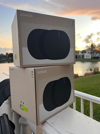 Dos bocinas Sonos Era 300 en sus cajas en una terraza junto al lago